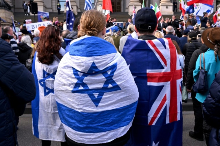 Des gens enveloppés du drapeau australien et israélien lors d'un rassemblement à Melbourne après une tentative d'incendie visant une synagogue dans la ville, le 6 juillet 2025 ( AFP / WILLIAM WEST )