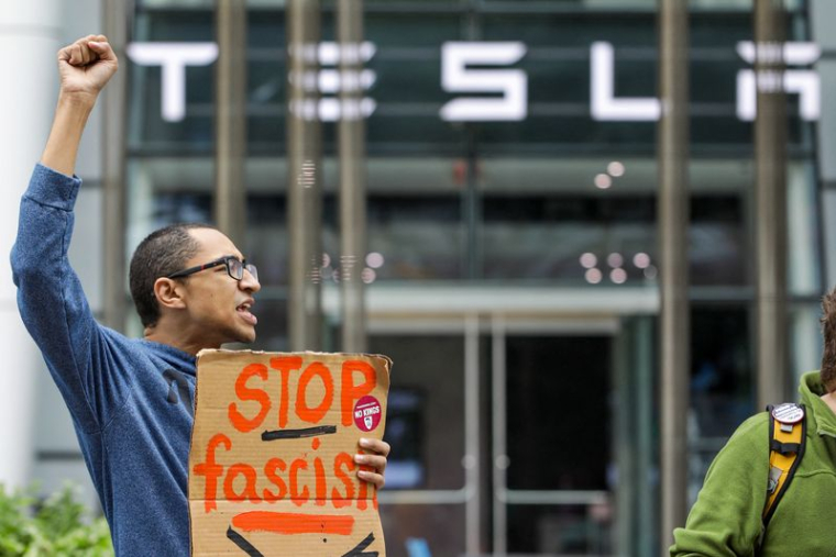 Sean Magrath lève le poing en signe de protestation lors d'une manifestation "Crappy Birthday Elon Protest" devant une salle d'exposition Tesla le jour de l'anniversaire du directeur général Elon Musk à Boston