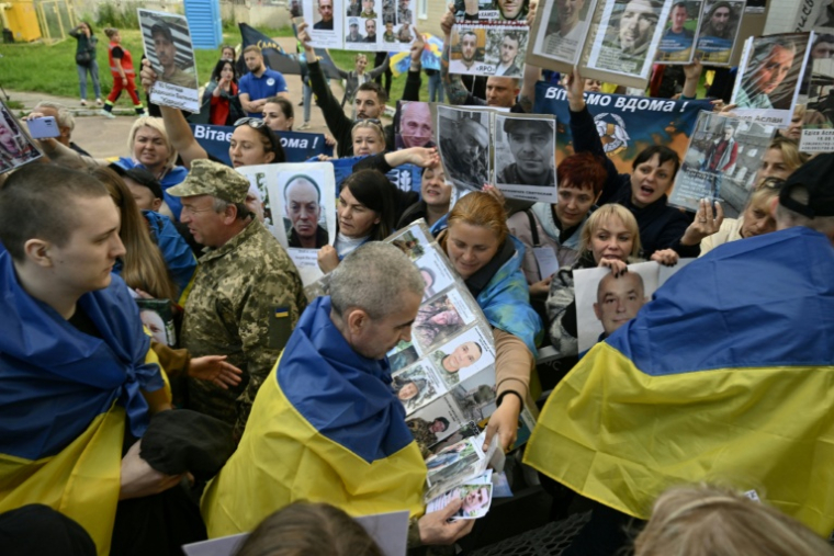 Des prisonniers de guerre ukrainiens libérés passent dans une foule brandissant des portraits de leurs proches disparus ou prisonniers des forces russes, le 26 juin 2025 dans la région de Tcherniguiv (Ukraine) ( AFP / Genya SAVILOV )