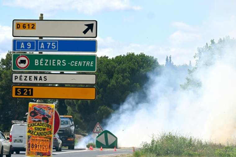 Des véhicules passent devant une route fermée alors qu'un incendie de forêt s'est déclaré près de Villeneuve-lès-Béziers, dans le sud de la France, le 7 juillet 2025 ( AFP / GABRIEL BOUYS )