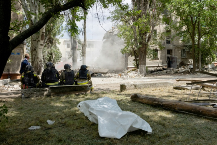 Des secouristes assis devant le corps d'une victime au pied d'un bâtiment effondré après une frappe russe à Kramatorsk, le 22 juin 2025 en Ukraine ( AFP / Tetiana DZHAFAROVA )
