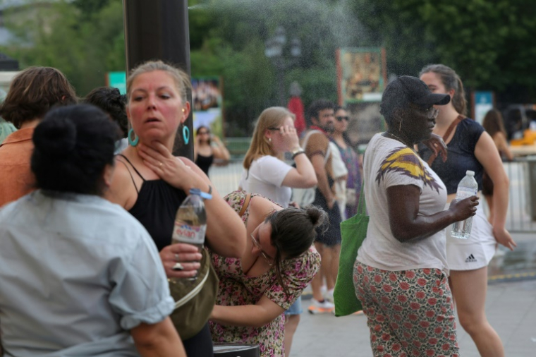 Des personnes se rafraîchissent en traversant un fin brouillard d'eau dans le centre de Paris le 21 juin 2025 ( AFP / ROMAIN PERROCHEAU )