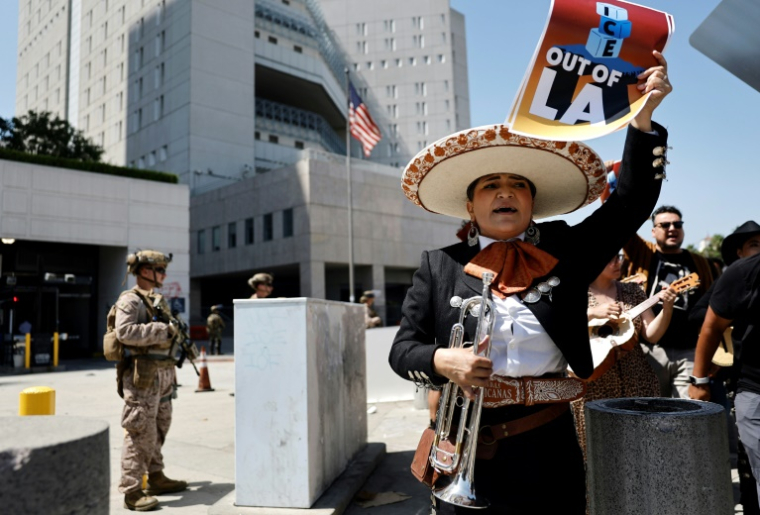 Une mariachi brandit une affiche réclamant le départ de la police de l'immigration de Los Angeles, devant un soldat montant la garde devant un bâtiment fédéral de la mégapole californienne, le 20 juin 2025 ( GETTY IMAGES NORTH AMERICA / MARIO TAMA )