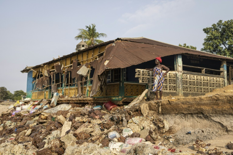Une habitante de l'île de Plantain devant un bâtiment abritant une mosquée menacée par l'érosion côtière, le 28 avril 2025 au large de la Sierra Leone ( AFP / PATRICK MEINHARDT )