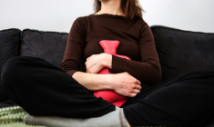 Une femme souffrant de règles douloureuses tient une bouillotte contre son ventre, assise sur un canapé à Toulouse, le 1er mars 2023 ( AFP / Charly TRIBALLEAU )