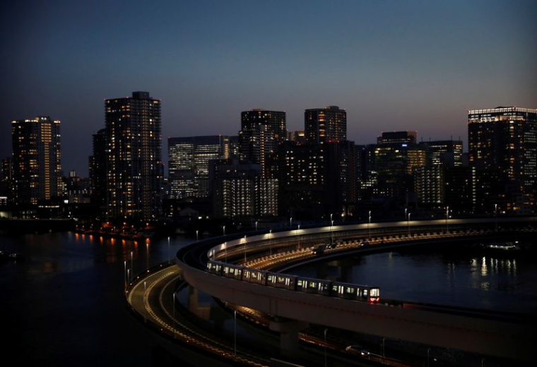 Un train de la ligne Yurikamome circule avec la silhouette urbaine en arrière-plan, à Tokyo