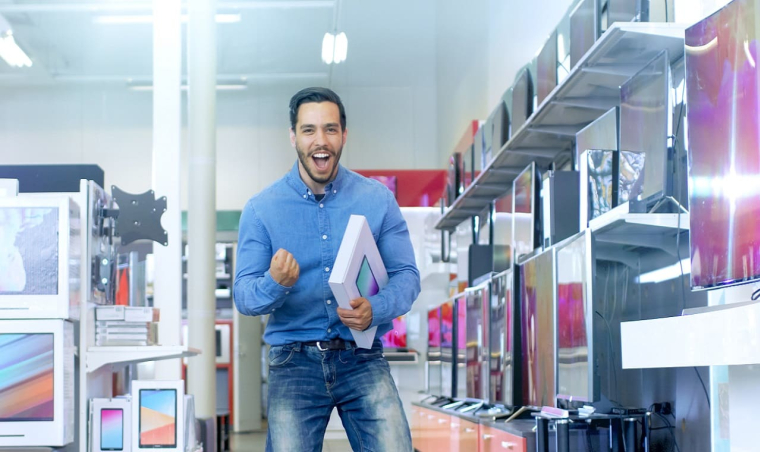 (Crédits photo : Adobe Stock - Homme se réjouissant d'avoir fait une bonne affaire pendant les soldes en achetant une tablette en magasin)