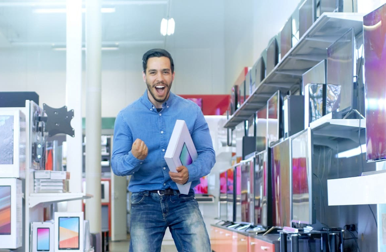 (Crédits photo : Adobe Stock - Homme se réjouissant d'avoir fait une bonne affaire pendant les soldes en achetant une tablette en magasin)