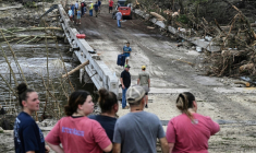 Des gens observent les forces de l'ordre et les volontaires qui recherchent des disparus près de Camp Mystic, le site où au moins 20 filles ont disparu après des inondations soudaines à Hunt, au Texas, le 5 juillet 2025 ( AFP / RONALDO SCHEMIDT )