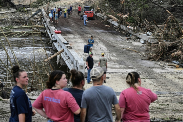 Des gens observent les forces de l'ordre et les volontaires qui recherchent des disparus près de Camp Mystic, le site où au moins 20 filles ont disparu après des inondations soudaines à Hunt, au Texas, le 5 juillet 2025 ( AFP / RONALDO SCHEMIDT )
