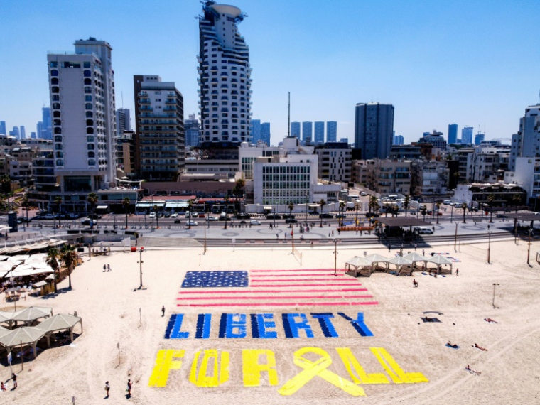 Un drapeau américain dessiné sur une plage de Tel-Aviv devant un bâtiment de l'ambassade des Etats-Unis, accompagné des mots "Liberté pour tous" pour réclamer la libération des otages retenus à Gaza, le 4 juillet 2025, jour anniversaire de l'indépendance des Etats-Unis ( AFP / Jack GUEZ )