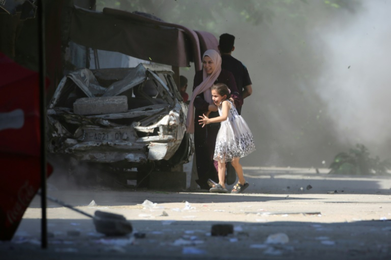 Une Palestinienne et sa fille se précipitent pour se mettre à l'abri lors d'une frappe israélienne dans le camp d'Al-Bureij, dans le centre de la bande de Gaza, le 4 juillet 2025 ( AFP / Eyad BABA )