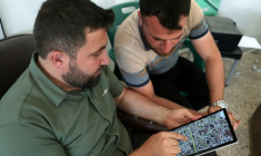 L'architecte syrien Abdel Aziz al-Mohammed (à gauche) montre sur une tablette une carte qu'il a créée, révélant l'état détaillé de chaque maison de son village de Tal Mardikh, dans la province d'Idlib, au nord-ouest de la Syrie, le 2 juin 2025 ( AFP / OMAR HAJ KADOUR )